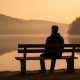 God’s Silence – a man sits alone on a bench by a calm lake at sunrise