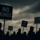 Protest crowd under a stormy sky holding “No Kings” signs during the No Kings Protest